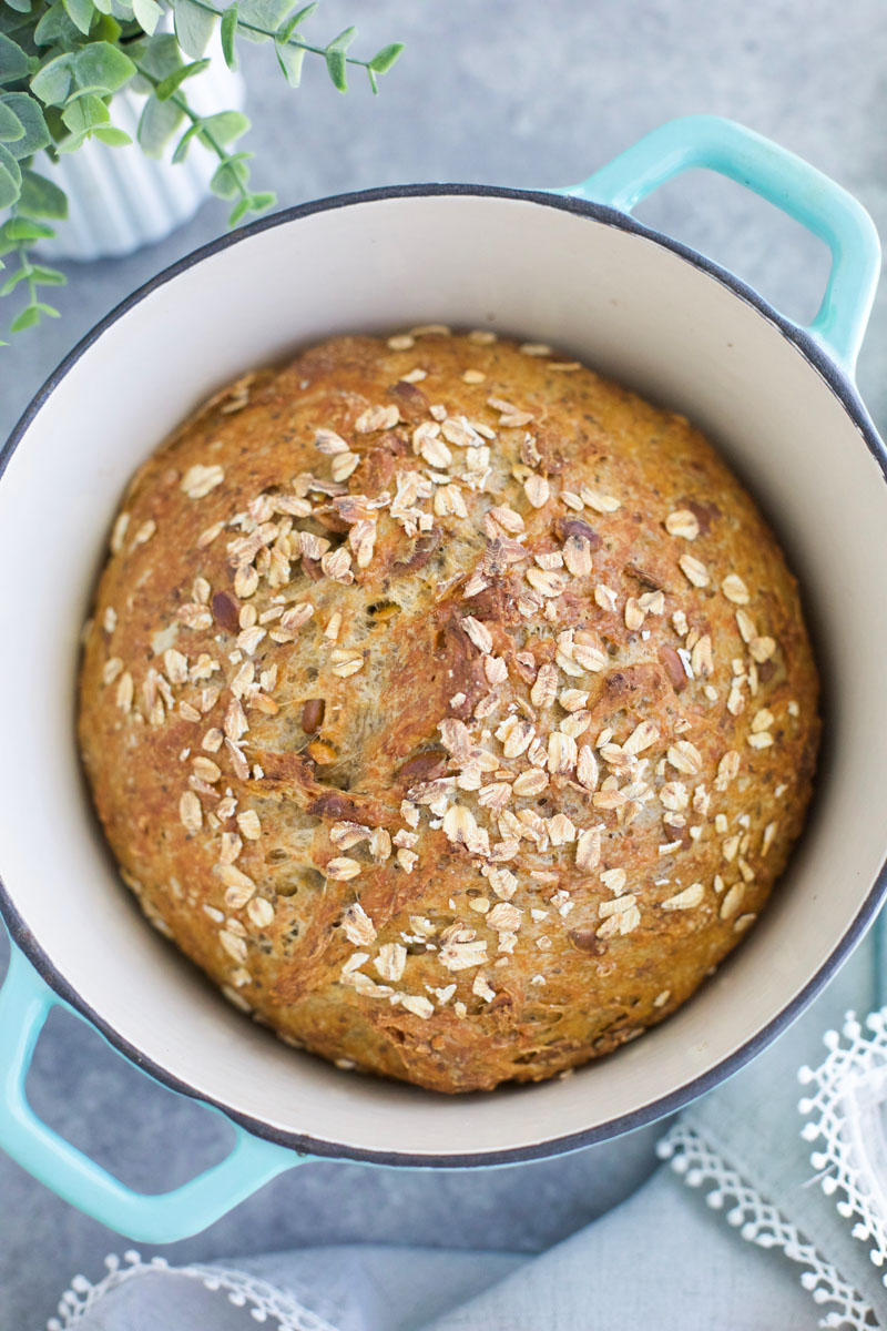 A baked loaf of vegan whole wheat bread in a aqua pot on a gray background. 