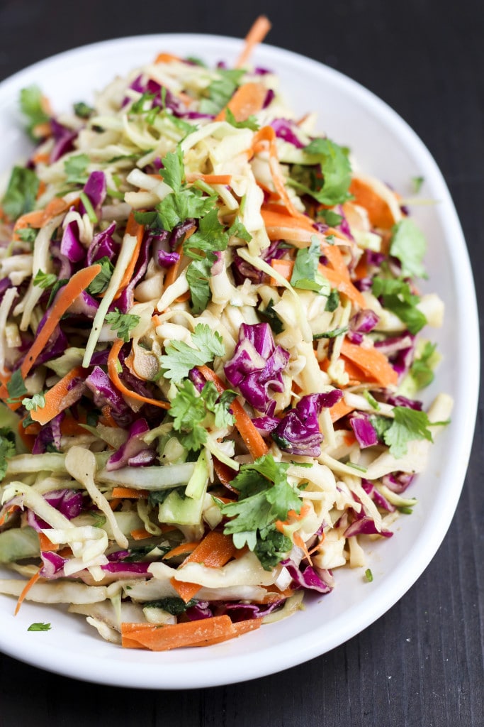 A white plate filled with vegan coleslaw on a dark wood background.