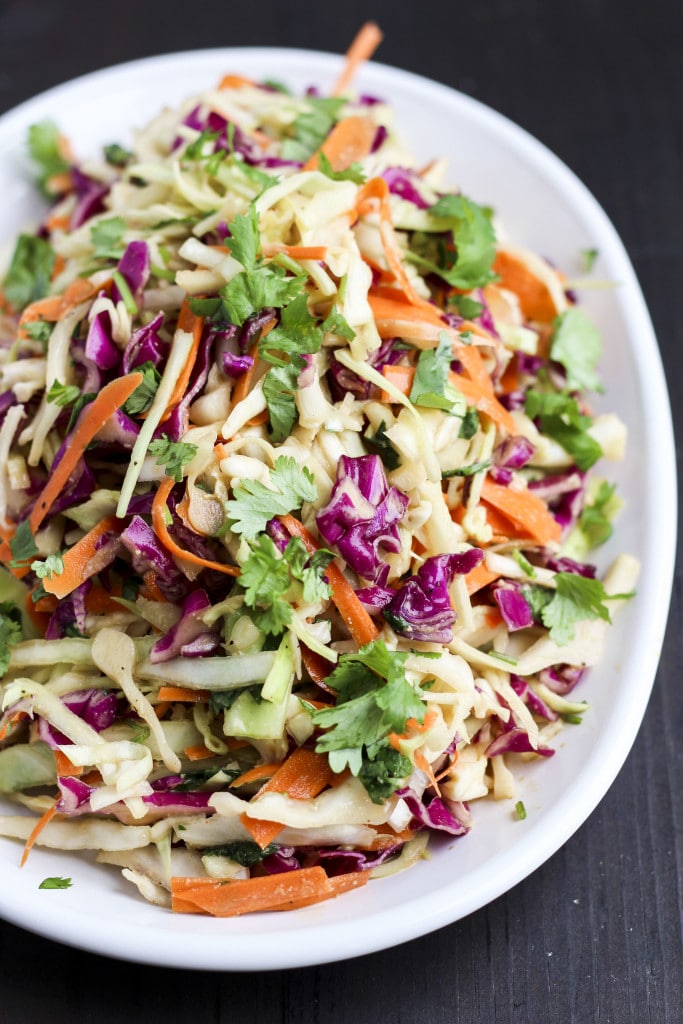 A white plate filled with vegan coleslaw on a dark wood background.