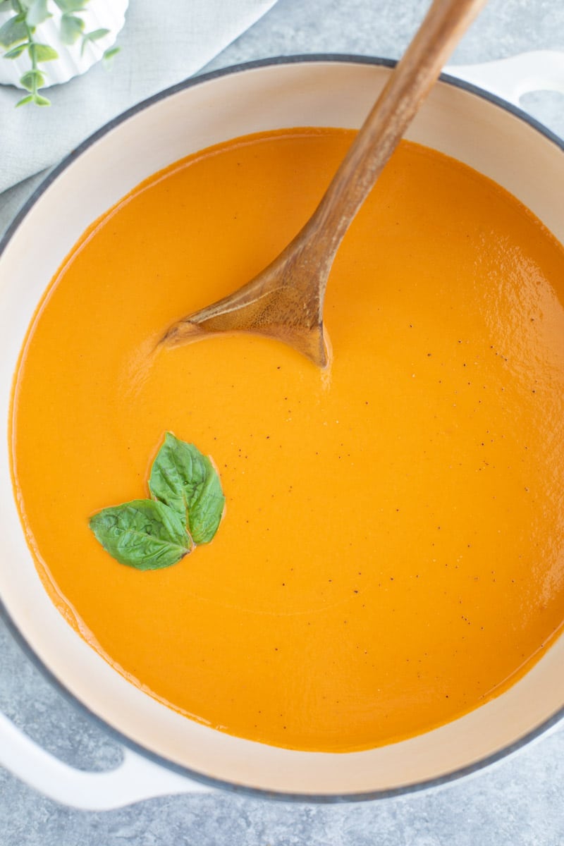 A large white post filled with soup, fresh basil leaves, and a wooden spoon.