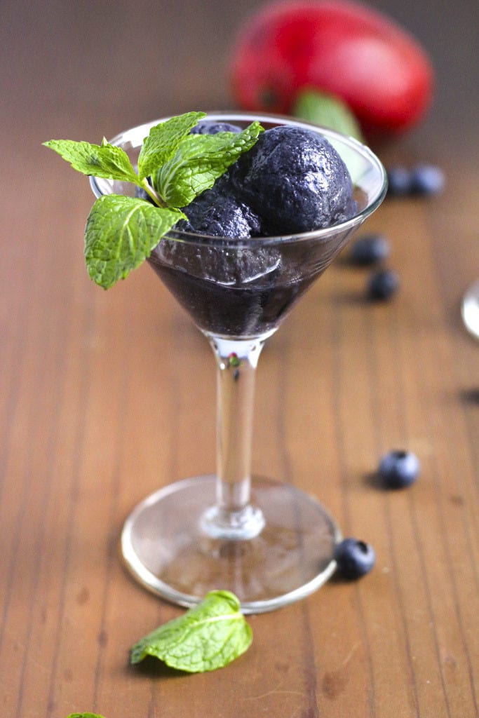 A martini glass filled with blueberry sorbet and fresh mint on a rustic background. 