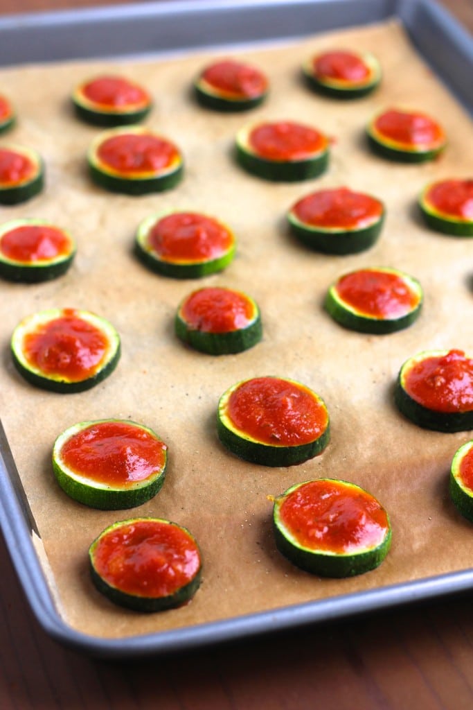 A large baking tray filled with zucchini slices that are topped with tomato sauce.