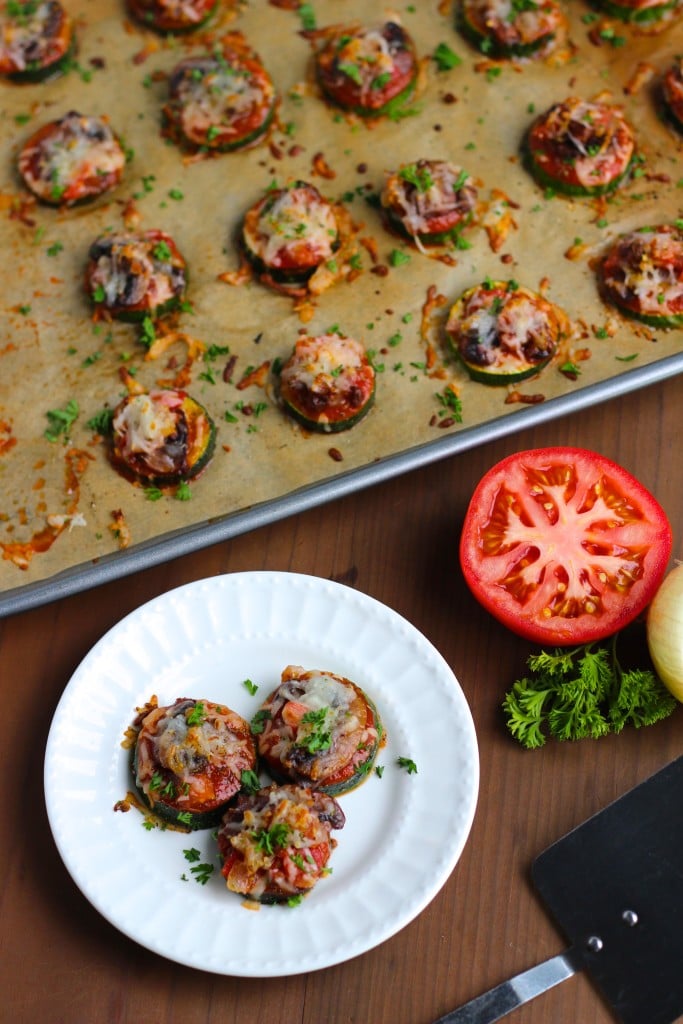 Vegan pizza bites on a white plate and a parchment paper lined tray.