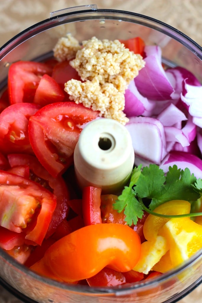 A food processor bowl filled with the ingredients to make salsa. 