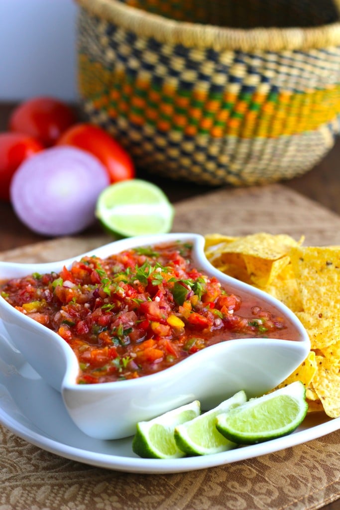 A white bowl of cilantro lime salsa with chips and lime wedges on top of a white plate.