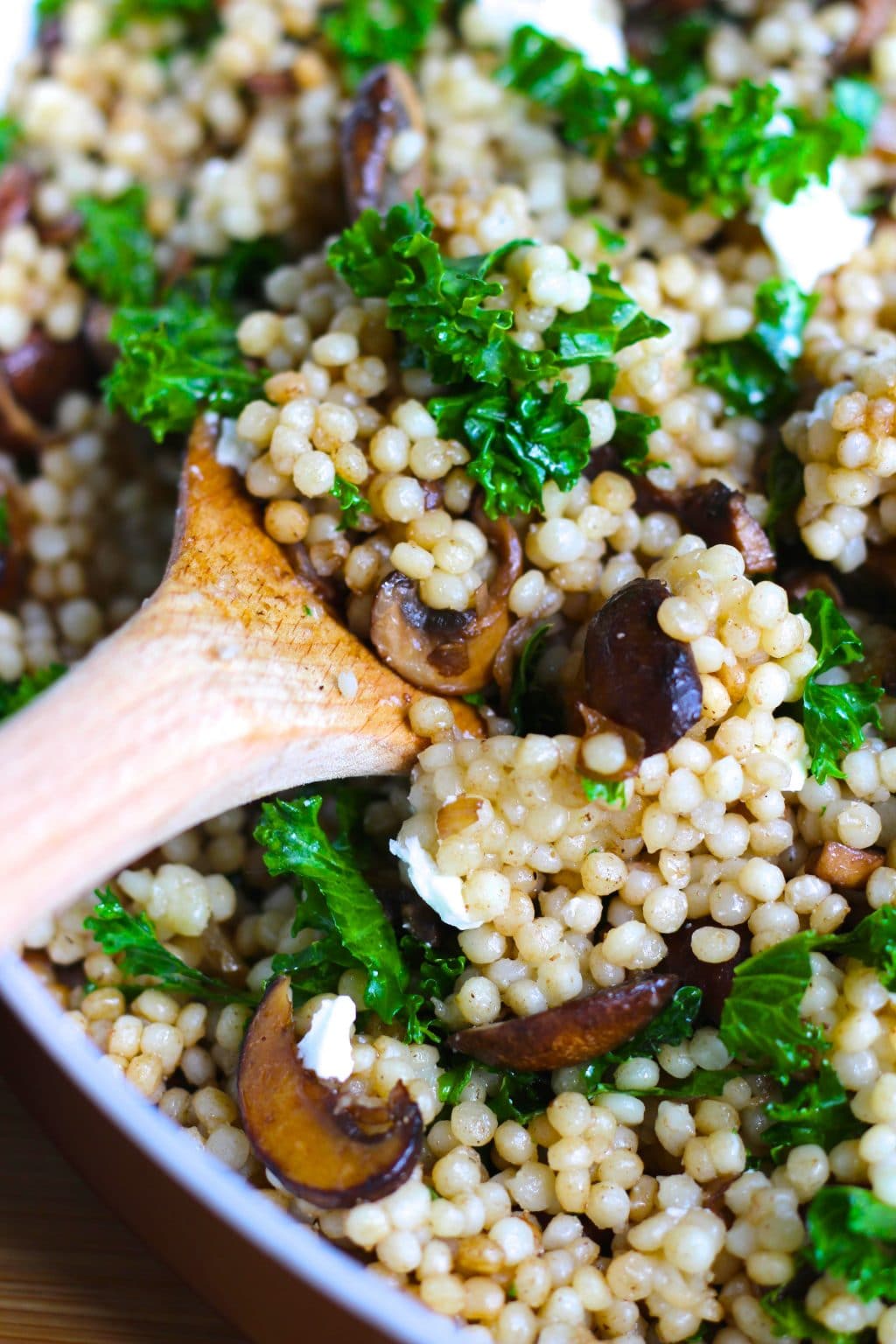 A wooden spoon scooping mushroom couscous out of a pan.