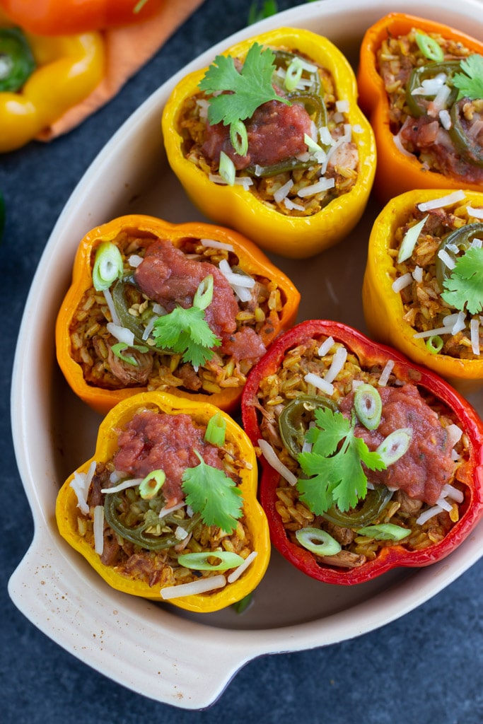A casserole dish filled with 6 multicolor meatless stuffed peppers sitting on a textured background.