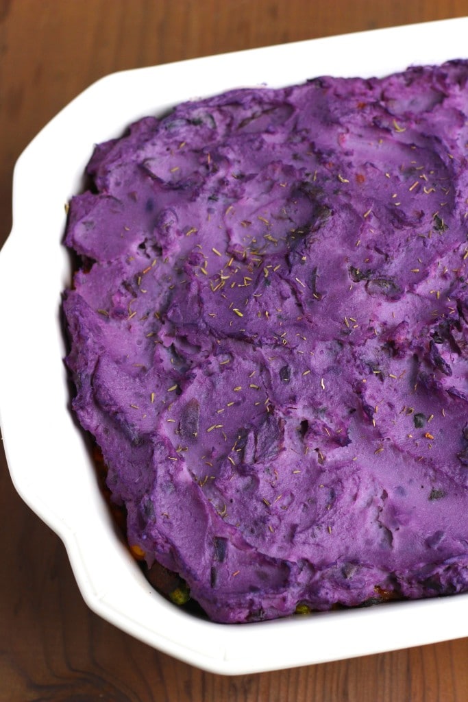 A white casserole dish filled with purple sweet potatoes on a rustic background. 