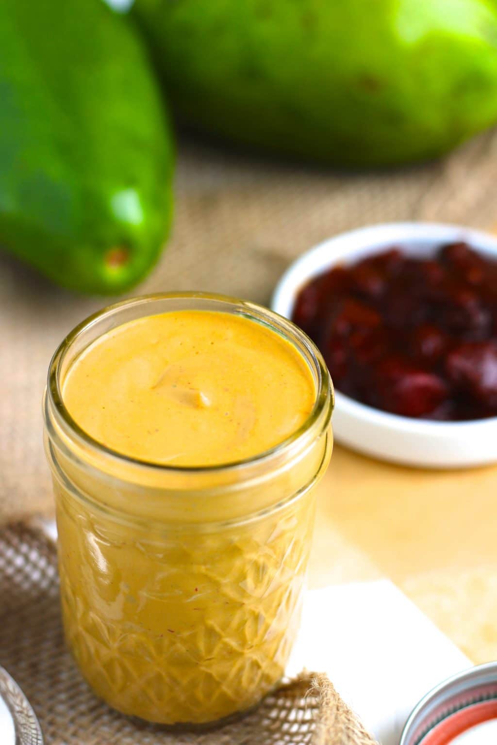 A small glass jar filled with chipotle mayo next to peppers and avocados. 