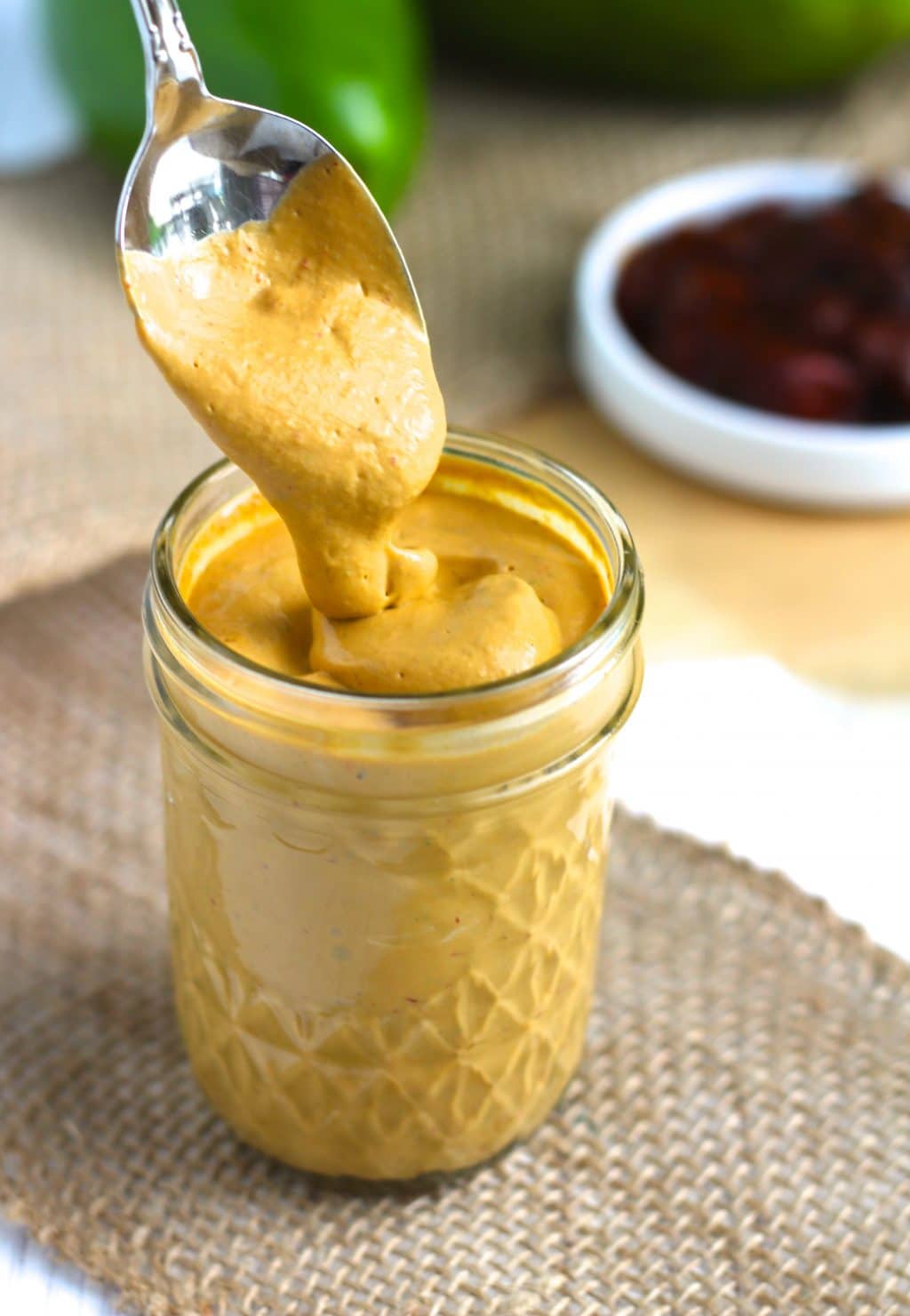 A spoon dipping into a jar of sauce on top of a piece of burlap.