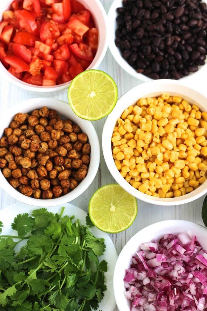 Six small white bowls filled with taco salad ingredients and a lime cut in half on a white background.