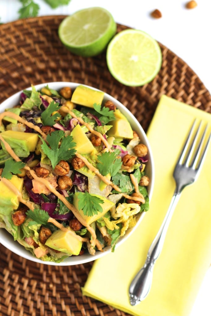 A white bowl filled with chickpea taco salad on a brown place mat next to a yellow napkin and a lime. 