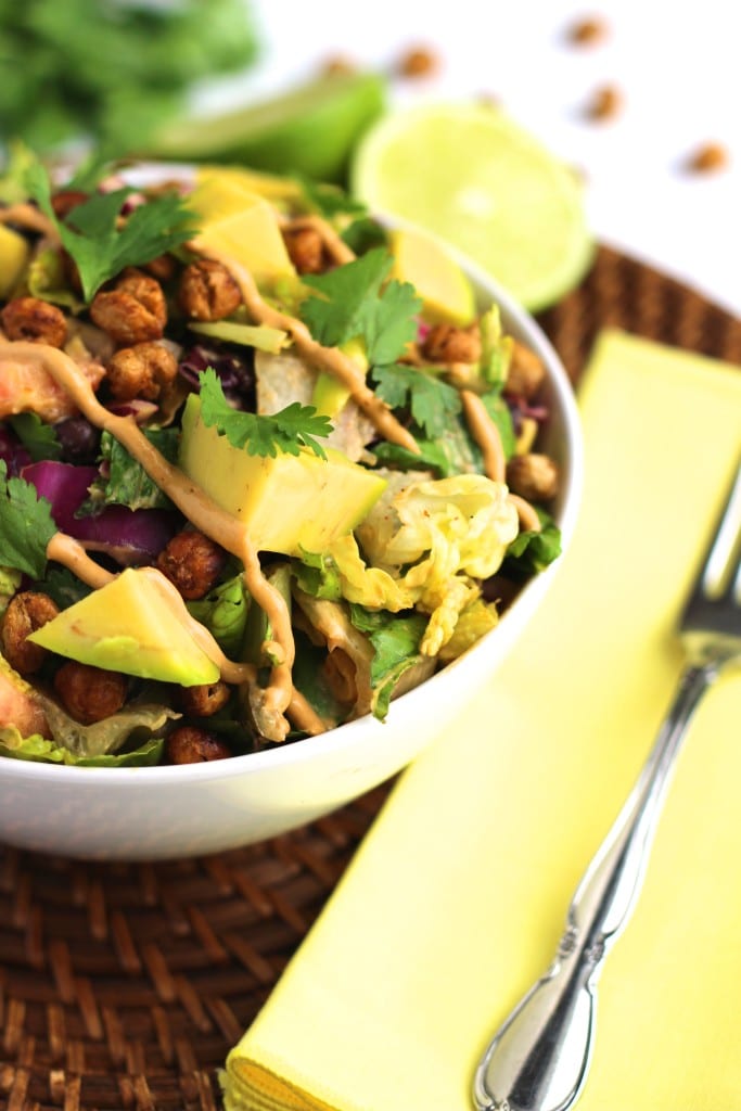 A white bowl filled with salad on a brown place mat next to a fork on a yellow napkin.