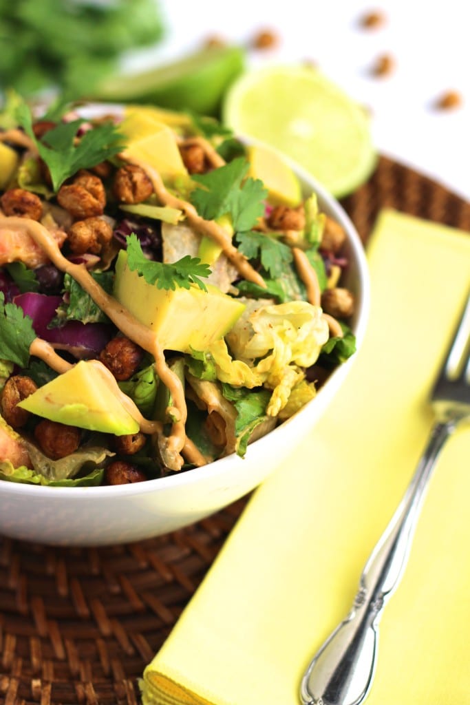 A white bowl filled with salad on a brown place mat next to a fork on a yellow napkin.