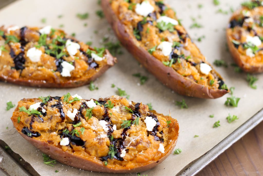 A tray filled with savory stuffed sweet potatoes that are topped with goat cheese, balsamic glaze, and parsley. 