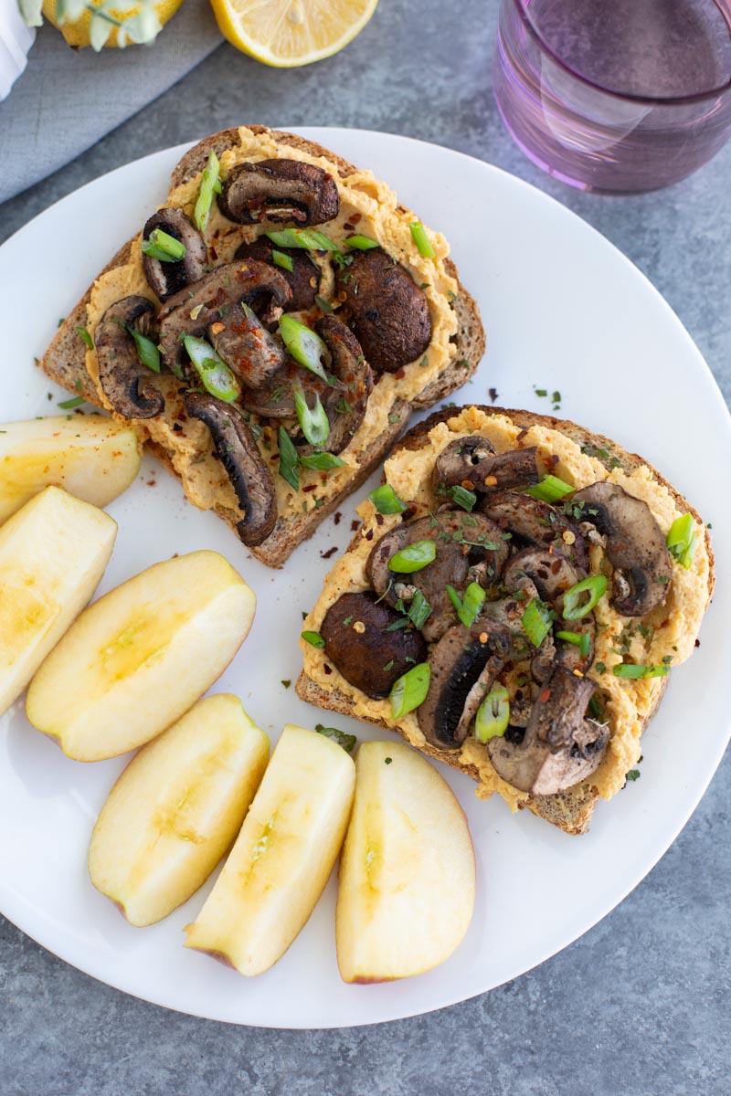 Two pieces of toast and sliced apples on a white plate on a gray background. 