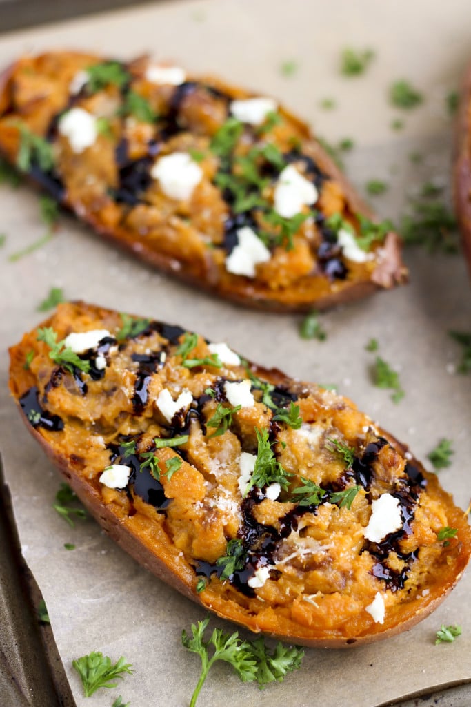 Two stuffed sweet potatoes topped with goat cheese and balsamic glaze on a piece of parchment paper. 
