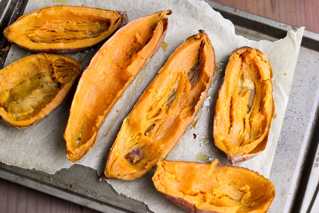 A baking tray filled with six sweet potato halves that have been scooped out.