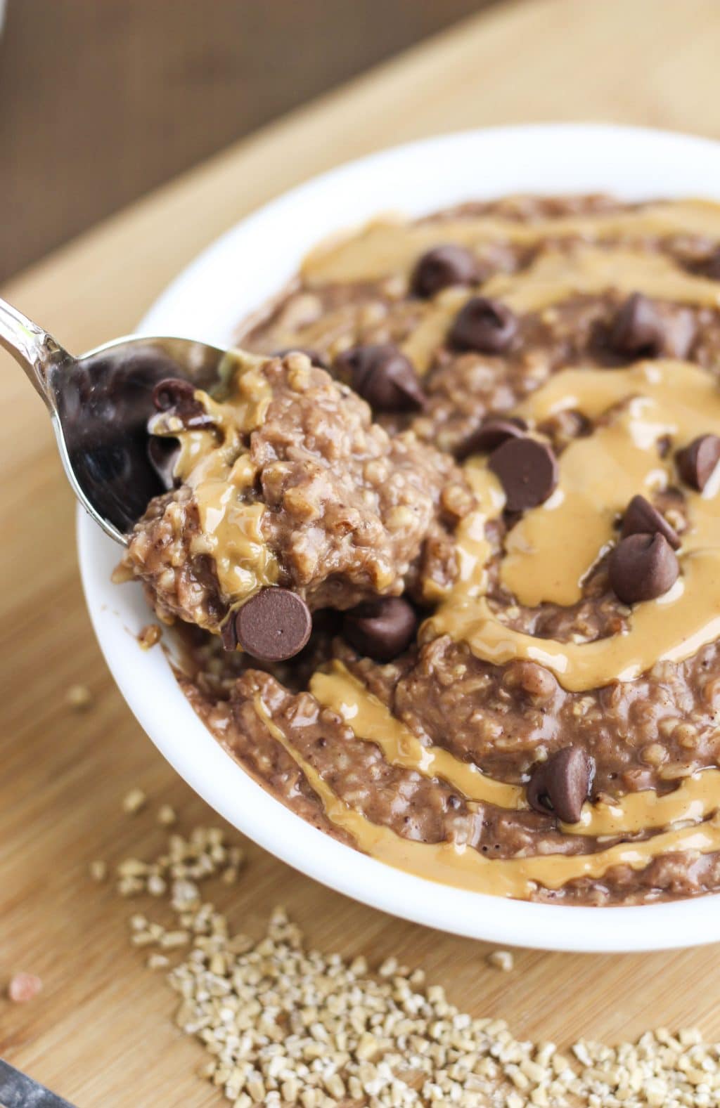 A spoon dipping into a bowl of vegan oatmeal on top of a wood cutting board. 