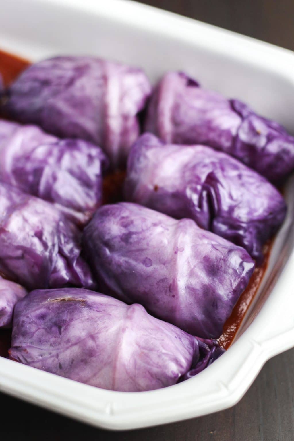 A white casserole dish filled with cabbage rolls in tomato sauce on a rustic background.