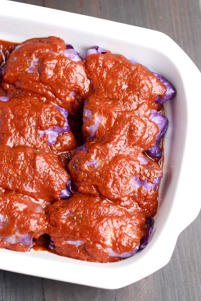 Ccabbage rolls covered in tomato sauce in a white casserole dish on a rustic background.