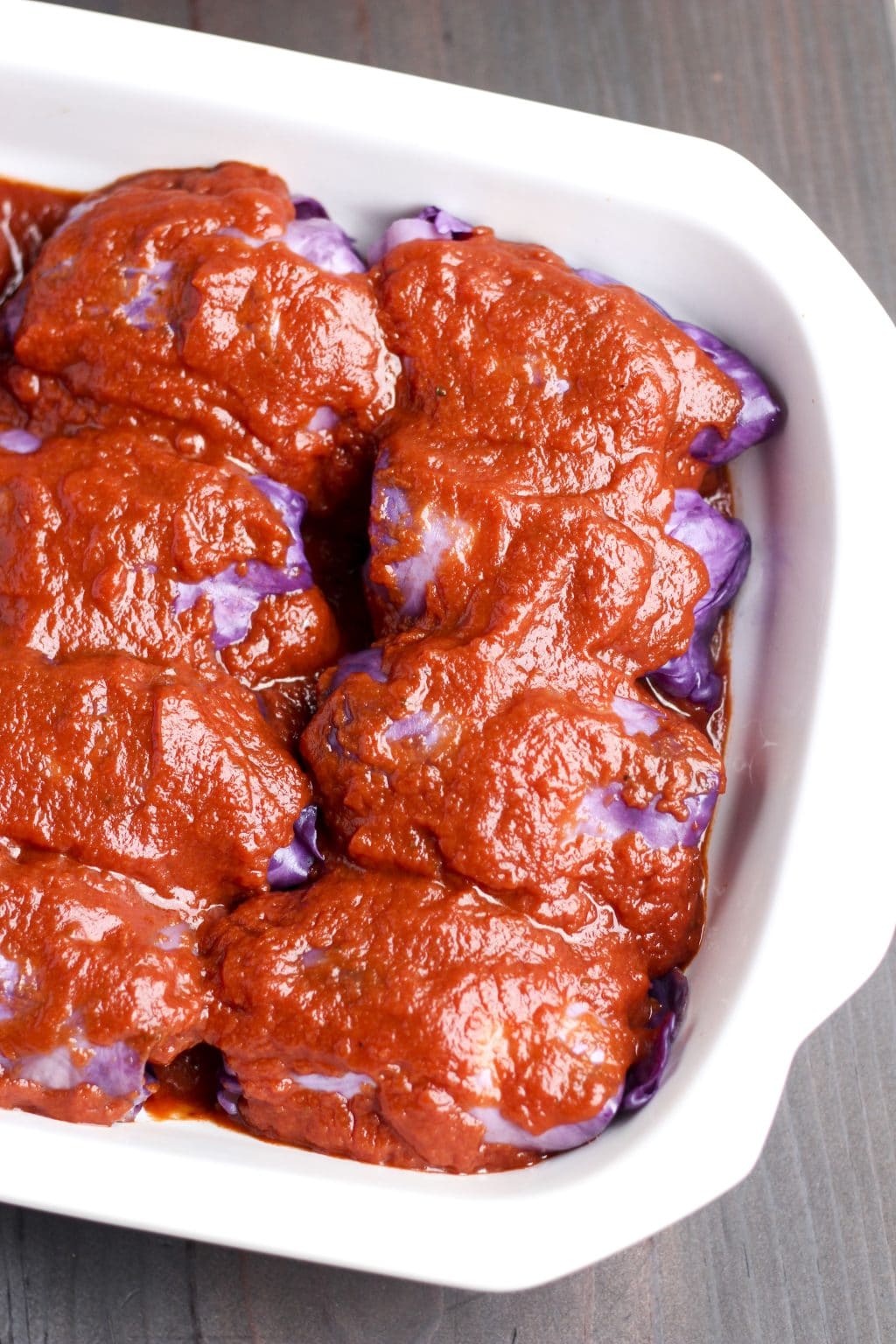 Cabbage rolls covered in tomato sauce in a white casserole dish on a rustic background.