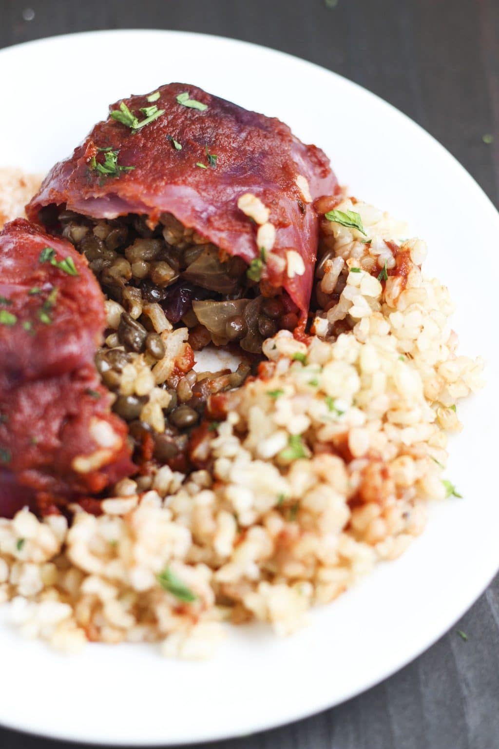 A cabbage roll cut in half so you can see the filling spilling out onto a white plate on a rustic background.