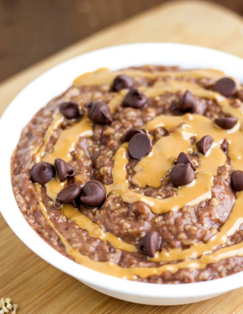 A white bowl filled with oatmeal topped with peanut butter and chocolate chips. 