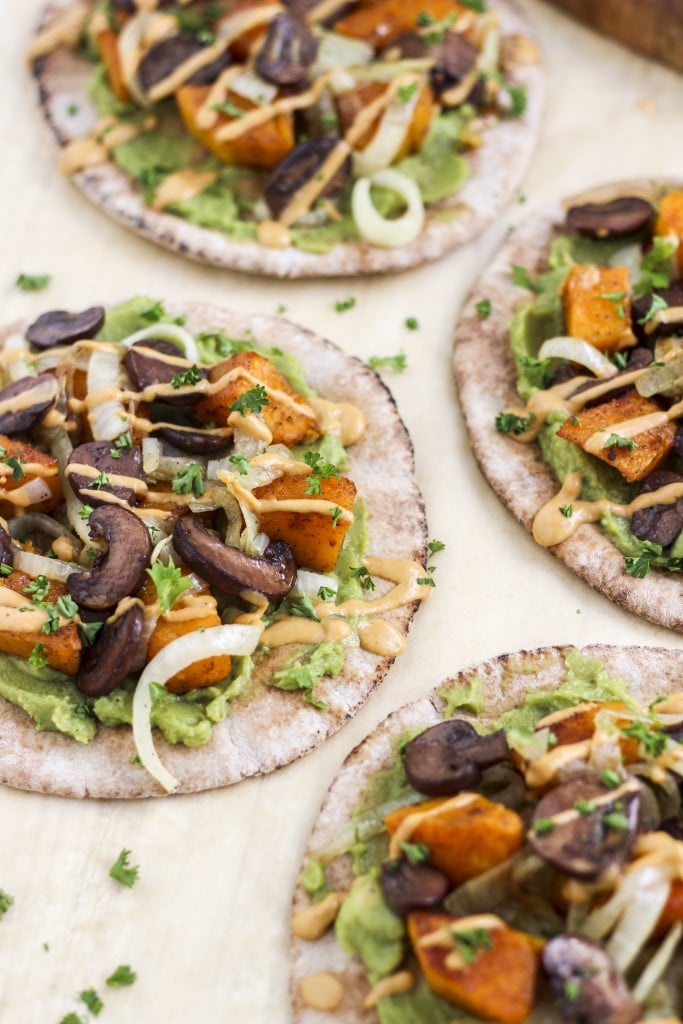 Multiple pita wraps topped with roasted vegetables and sauce on a light background. 