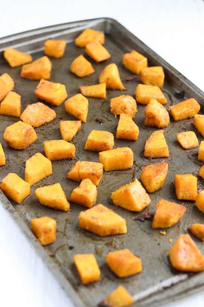 Chunks of seasoned butternut squash on a baking tray. 