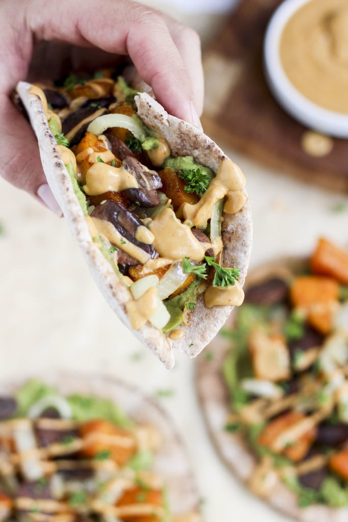 A hand holding a pita wrap filled with vegetables and chipotle mayo over a tray of pitas.