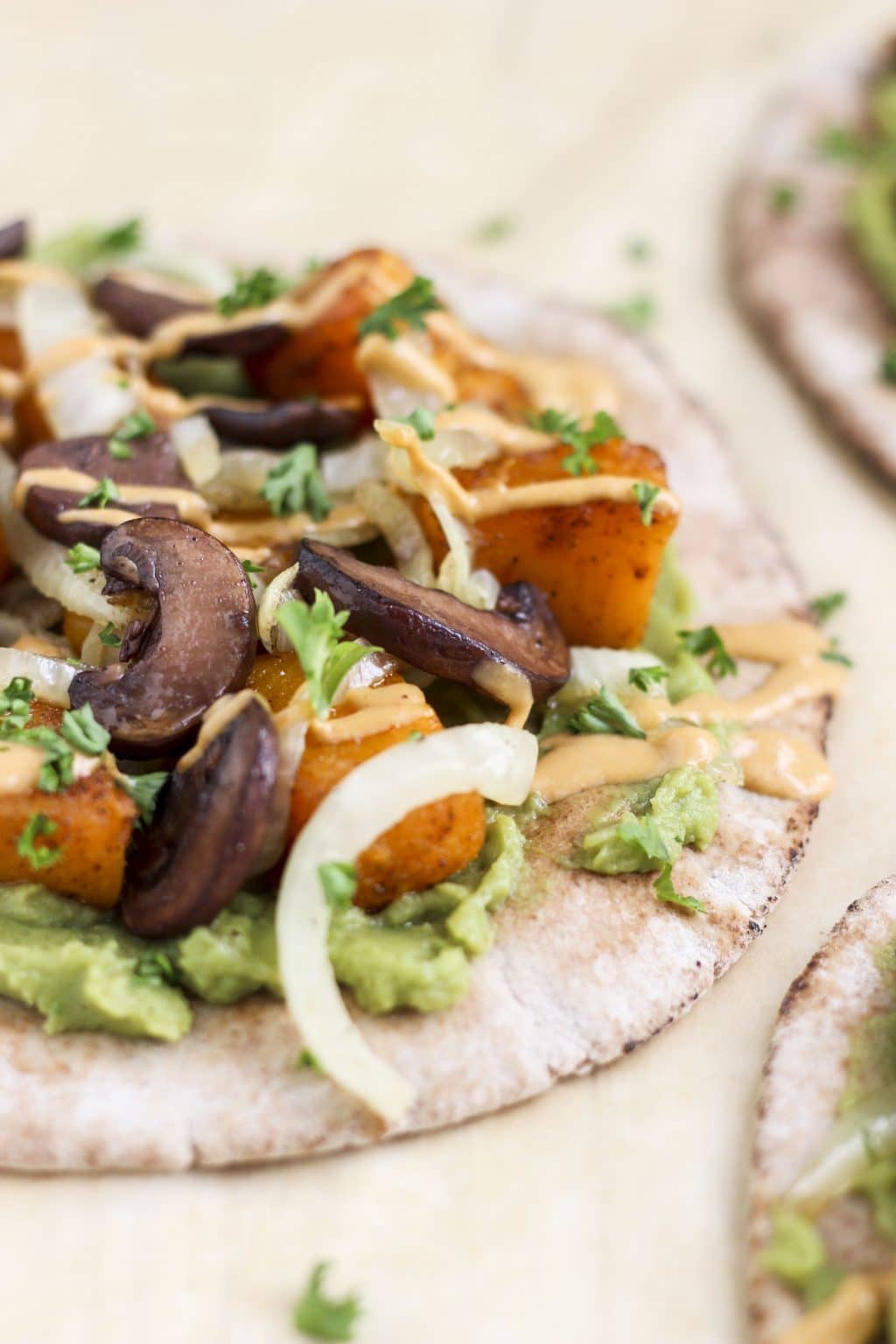 A close up view of a pita topped with roasted vegetables, mashed avocado, and sauce. 