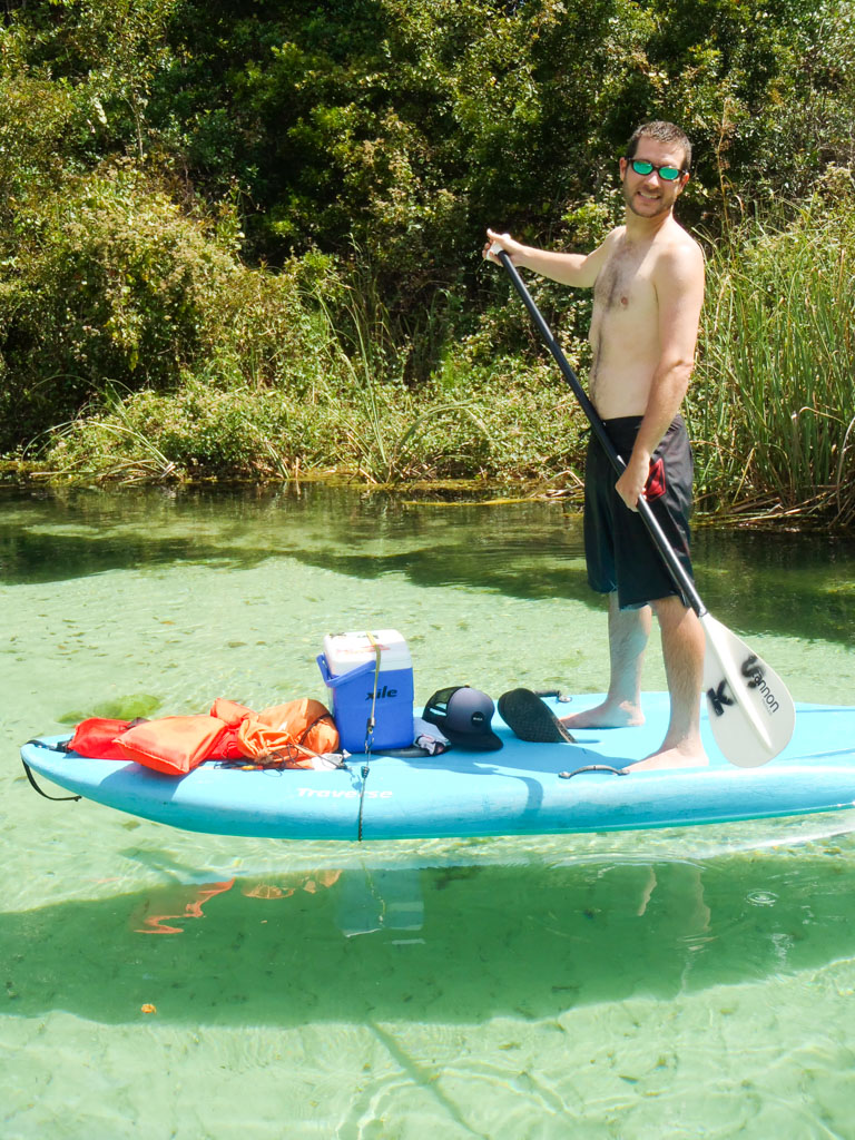 A young man stand up paddle boarding on a blue paddle board going up the Weeki Wachee river. 