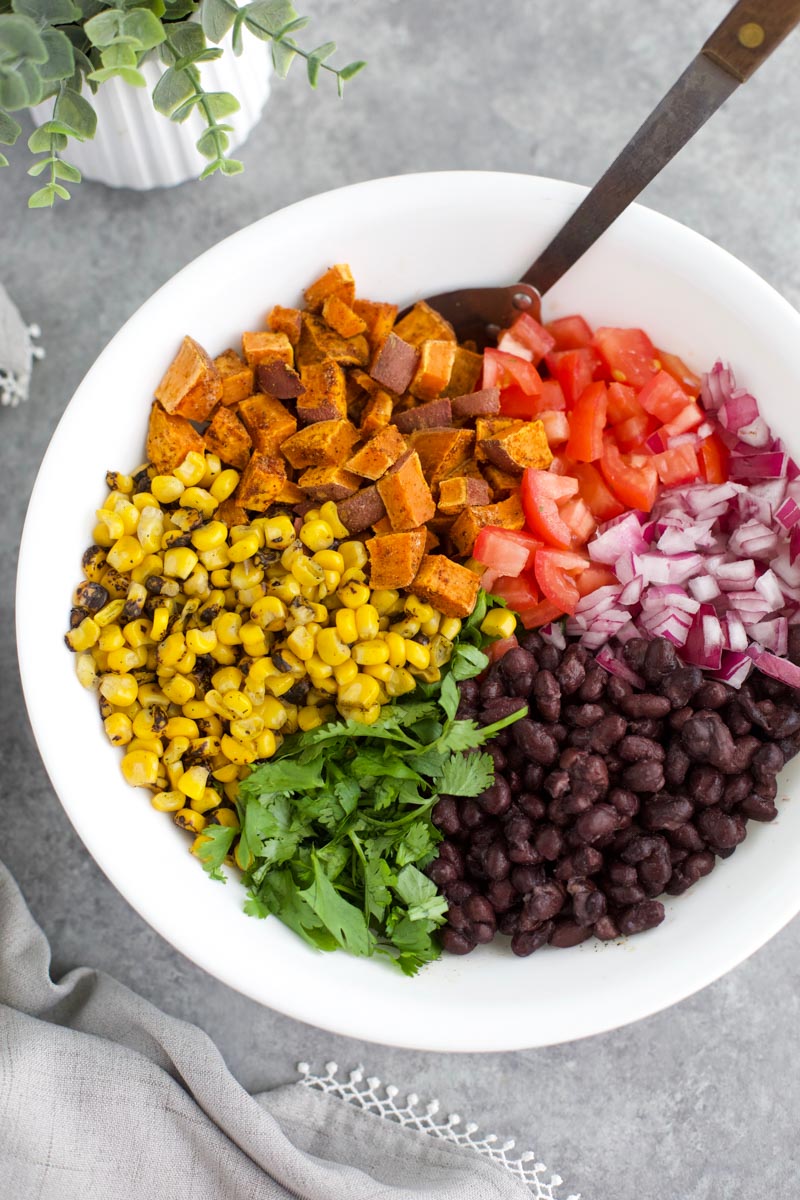 A white bowl filled with vegetables and a spoon on a gray background.