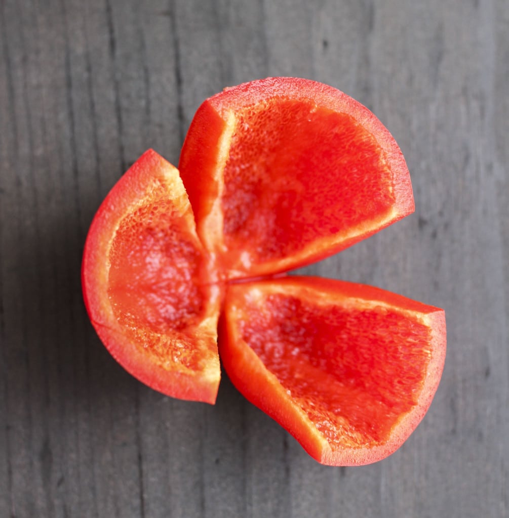 A red bell pepper sliced into wedges on a dark background. 