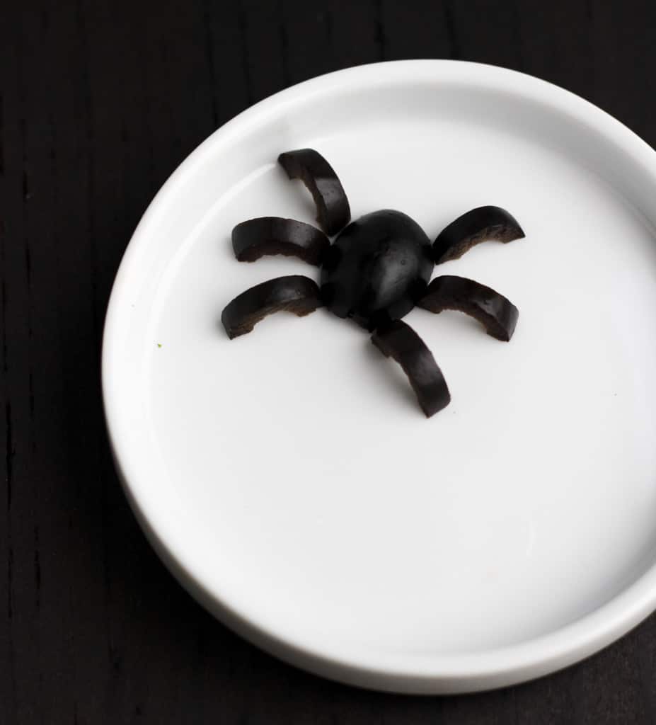 A black spider made of olives on a white plate with a dark background. 