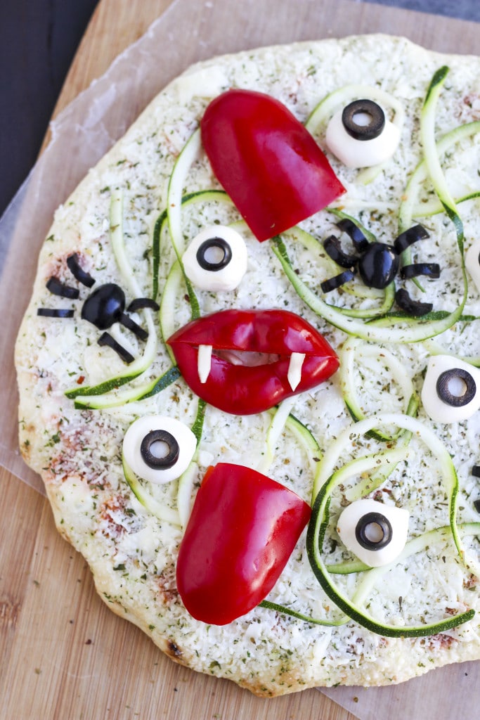 An unbaked frozen pizza topped with vegetables on top of a cutting board. 