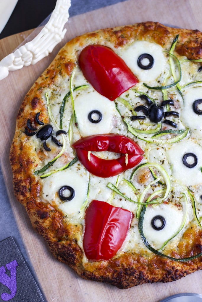 A baked pizza topped with spooky Halloween toppings on top of a cutting board. 