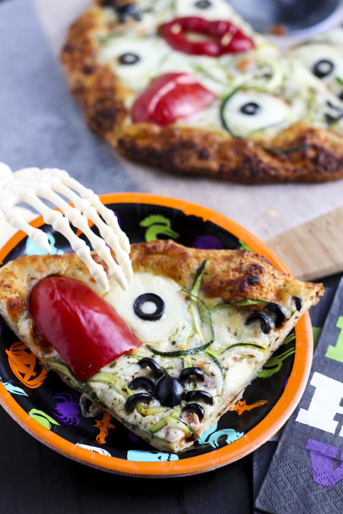 A skeleton hand grabbing a piece of pizza on a halloween-themed paper plate. 