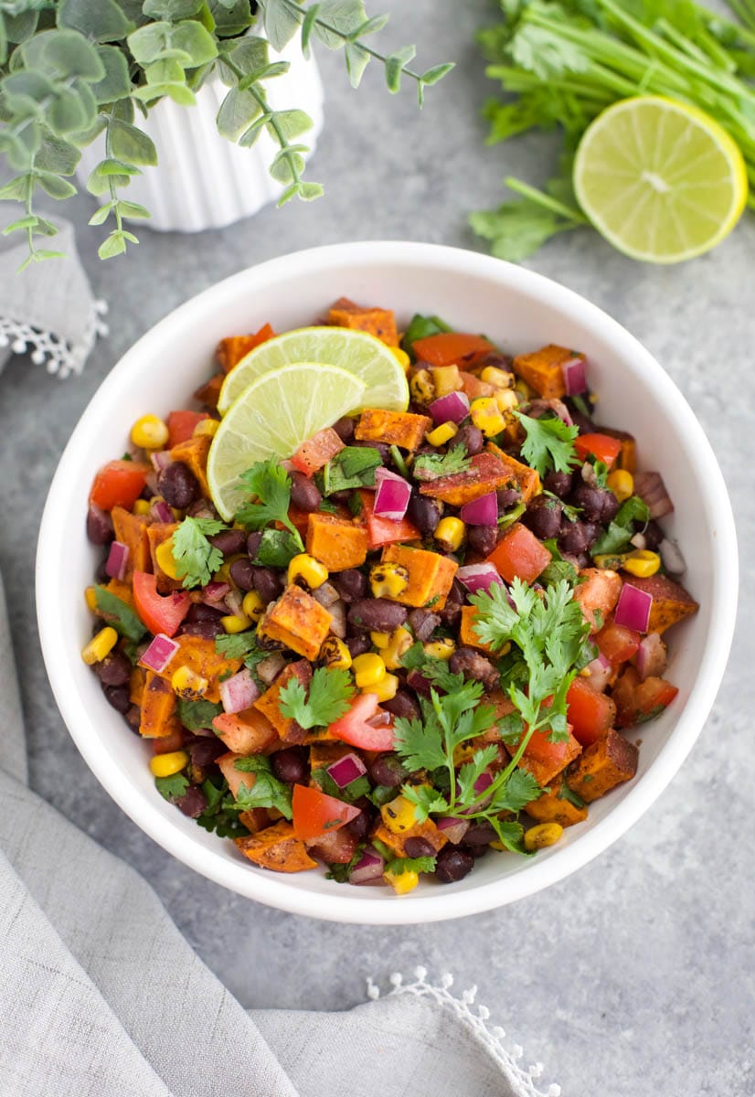 A white bowl filled with sweet potato salsa next to a lime on a gray background.