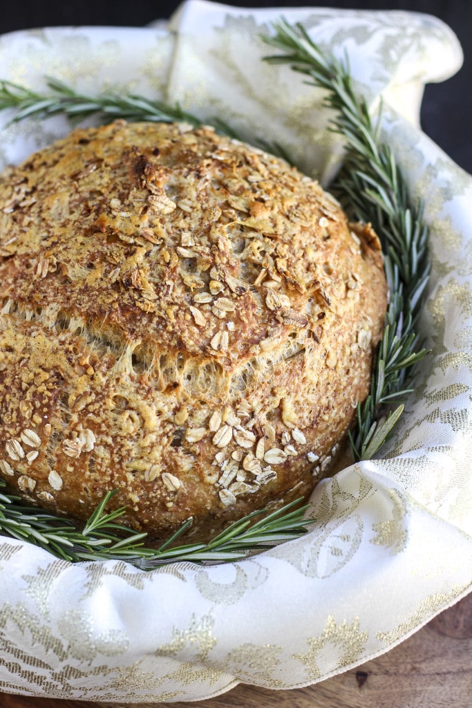 A loaf of vegan rosemary bread in a basket with a few sprigs of fresh rosemary. 