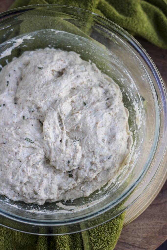 Bread dough in a large clear bowl on top of a green towel. 