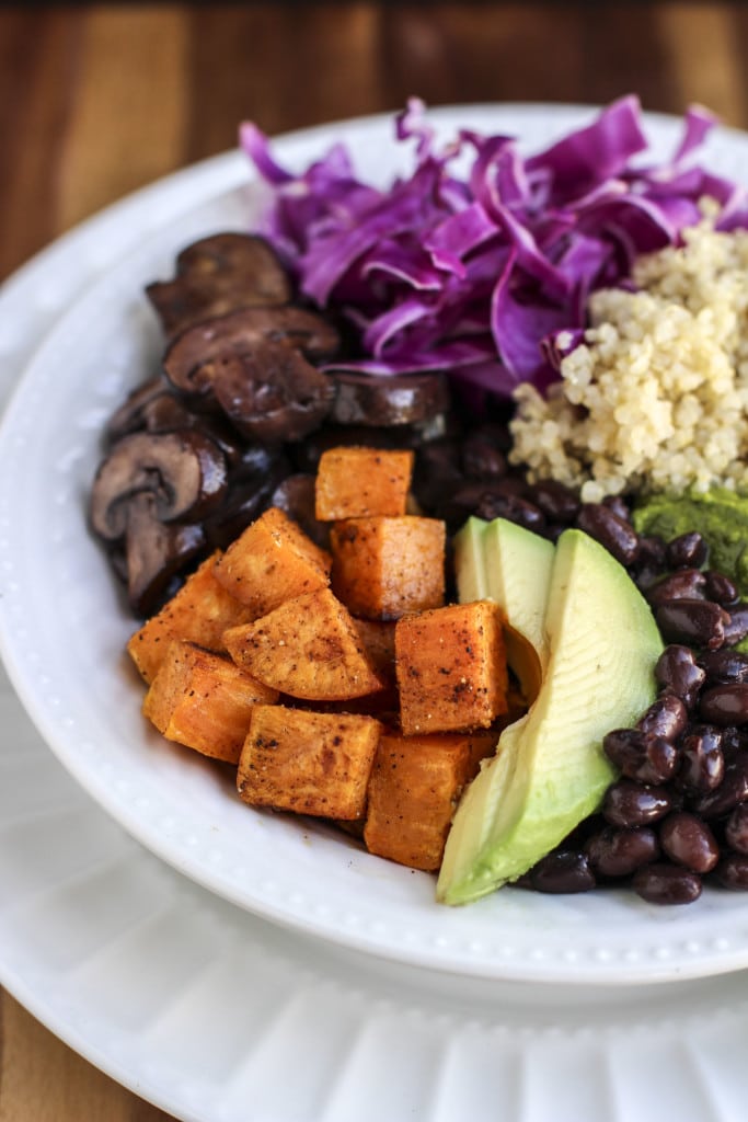 A side view of a white bowl filled with vegetables, beans, and quinoa on a rustic background.