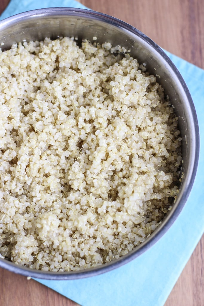 Cooked quinoa in a stainless pot on top of a teal napkin with a rustic background.