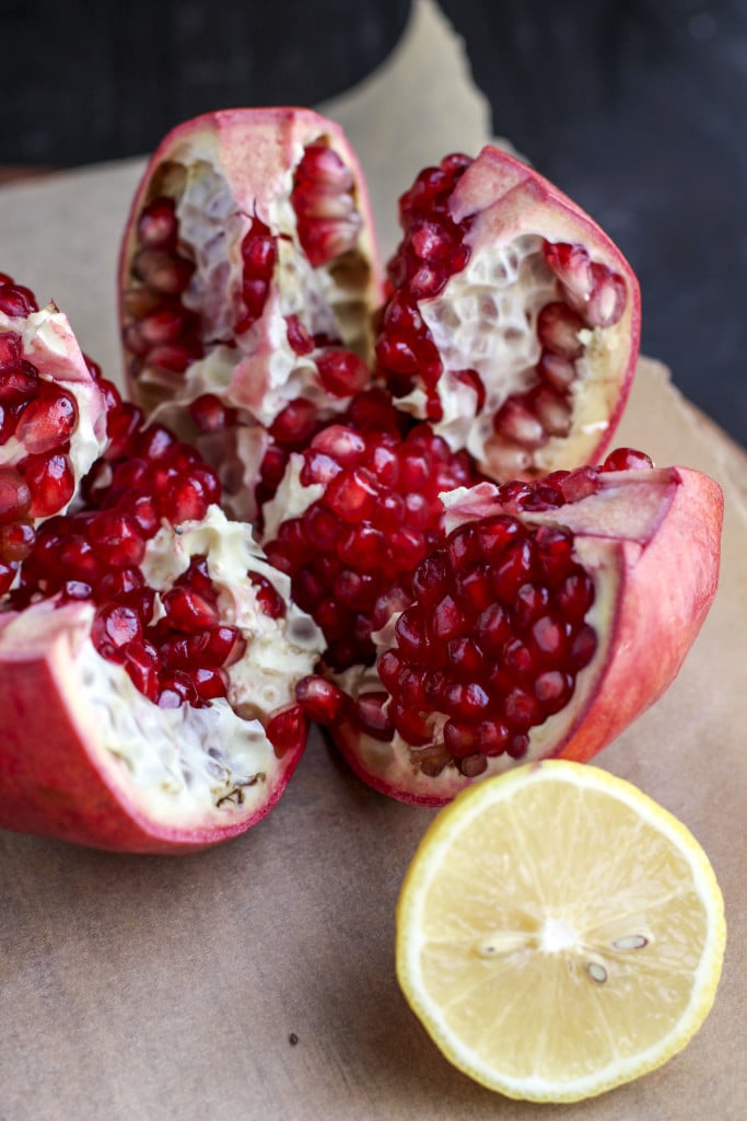 A pomegranate sliced into wedges next to a lemon on a piece of parchment. 