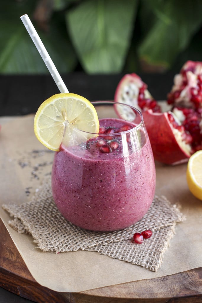 A pink lemon smoothie in a glass cup with a lemon wheel and straw on a piece of burlap.