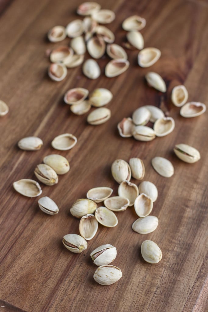 Pistachios scattered on top of a wooden cutting board.