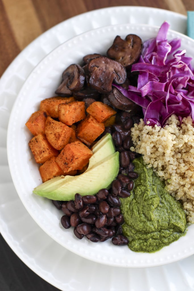 Overhead shot of a nourish bowl filled with vegetables, beans, quinoa, and green pistachio sauce on a rustic background.
