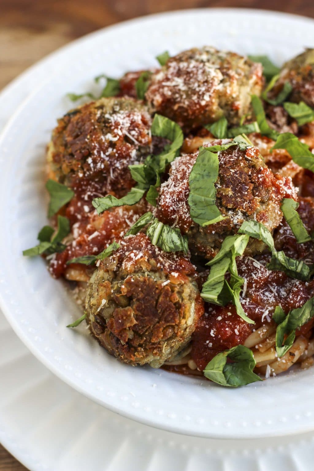 Vegan meatballs with fresh basil and spaghetti in a white bowl.