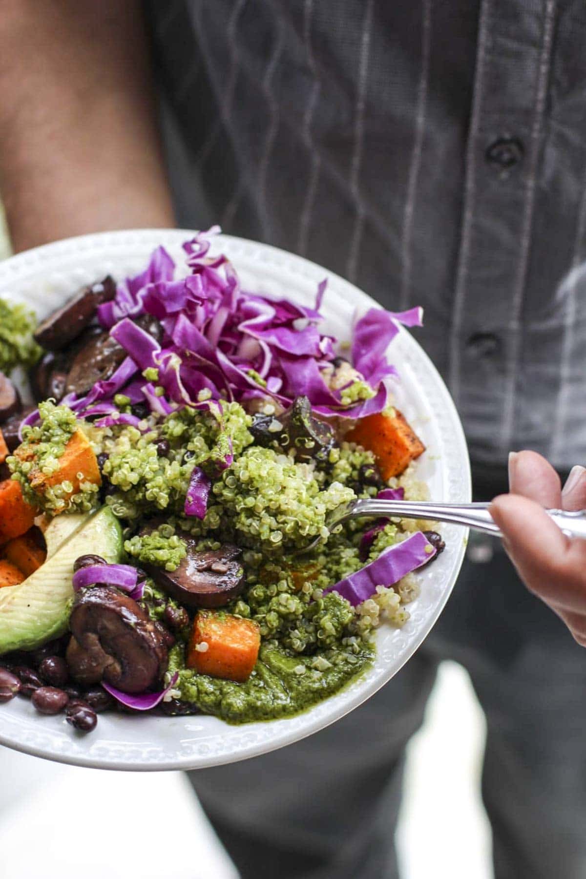 A man holding a white bowl filled with quinoa and vegetables.